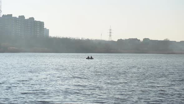 Lonely boat with two fishermen on the lake. Foggy lake with silhouette of a boat