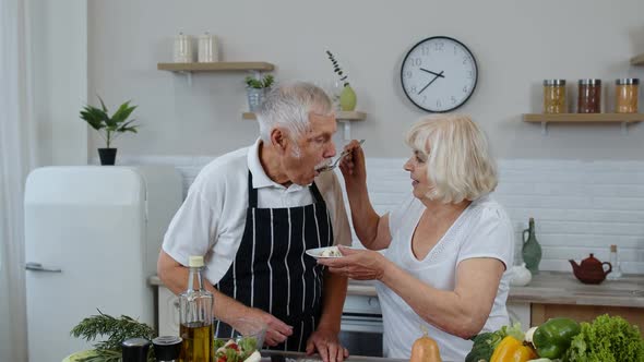 Senior Couple in Kitchen. Grandmother Feeding Grandfather with Raw Sprouts Buckwheat with Nuts