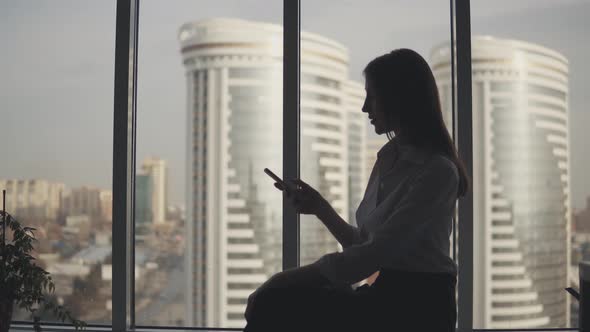 Silhouette of a Girl with a Phone in Her Hands on the Background of Modern Buildings. Business Woman