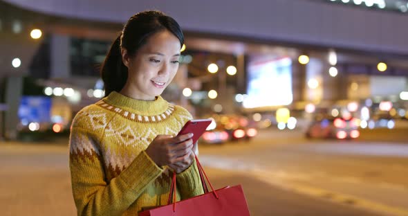 Woman use of mobile phone in city and hold with shopping bag at night