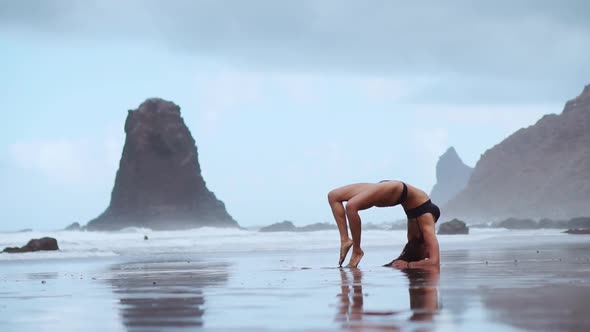 Girl Gymnast on the Beach Makes a Wheel and Becomes a Pose Bridge Standing on His Hands and Feet