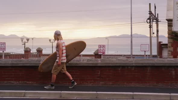 Caucasian male surfer holding a wooden surfboard and walking