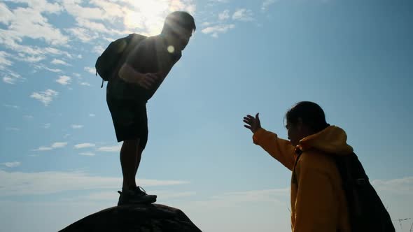 Silhouette of Asian couple climbing mountain, helping each other climb to the top of the mountain