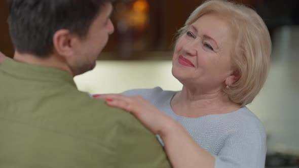 Portrait of Happy Senior Smiling Mother Dancing with Adult Son Listening Stories with Surprised