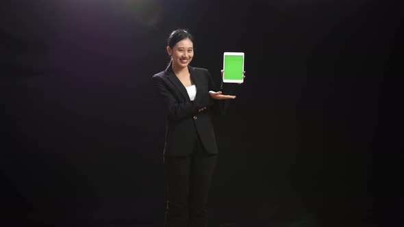 Speaker Woman In Business Suit Holding And Pointing Green Screen Tablet In The Black Screen Studio