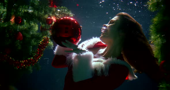 Beautiful Long-haired Girl in a Christmas Red Suit, She Is Under Water, Smiling, Next To Her Elegant