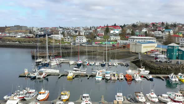 Sailboats And Fishing Boats Moored At Marina With Coastal Town Houses In The Background. - aerial