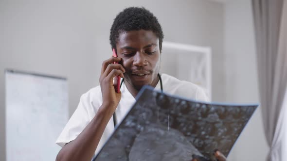 Young African American Doctor Consulting Colleague Talking on Phone Analyzing Brains Xray Image