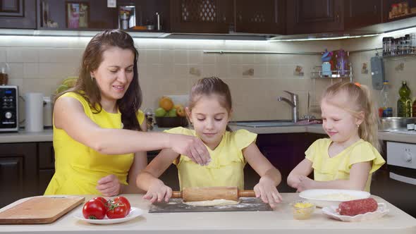 Mom and Children Cook in the Kitchen. Little Girl Smooths Pizza Dough. Mom Helps Children Cook Pizza
