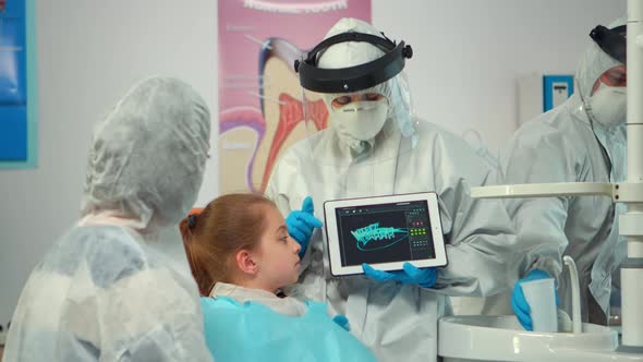 Dentist with Ppe Suit Pointing on Digital Screen Explaining Xray to Mother