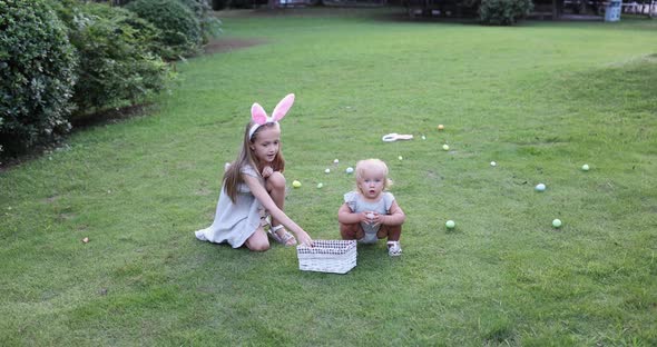 Two Children Wearing Bunny Ears When Pick Up Painted Easter Egg Hunt In Garden or Park