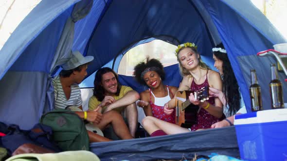 Friends singing song and playing guitar in tent