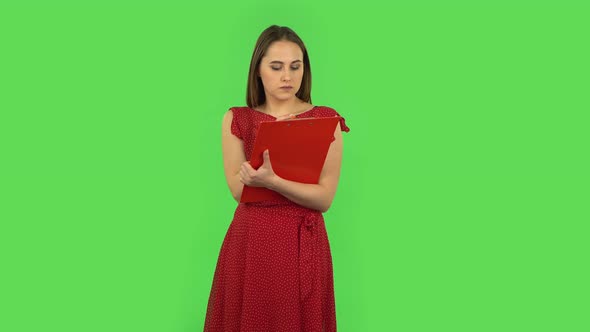 Tender Girl in Red Dress Fills Papers in Red Folder with Pensil. Green Screen