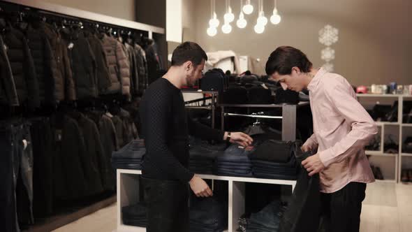 a Young Man Looks at Jeans for Purchase the Seller Helps Him