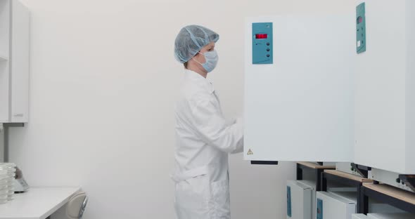 Female Scientist in White Coat Mask and Cap Using Large Fridge Unit in Lab