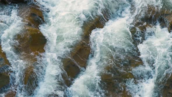 Aerial view of river waterfall with clear turquoise water falling down between wet boulders with