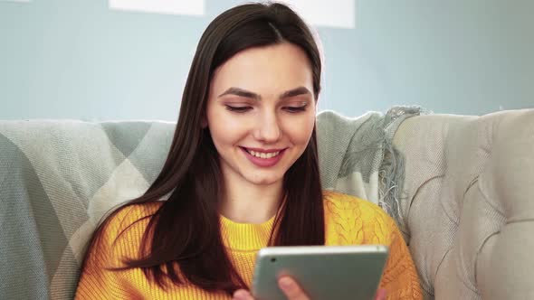 Woman Sitting on Cozy Sofa Smiles and Studies App on Digital Computer Tablet