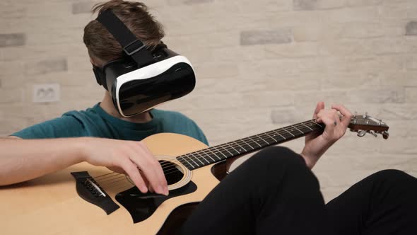 Young Man with the Virtual Reality Glasses Is Playing at the Guitar.