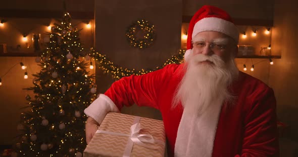 Santa Claus Stands in the Living Room Next To a Christmas Tree Then Takes a Box with a Present for
