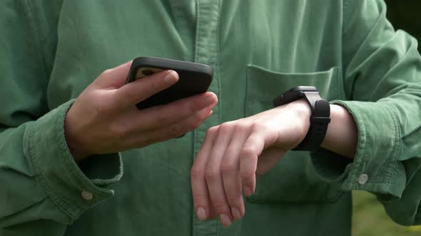 Stylish woman in green shirt check time and health indicators on wrist watch and mobile phone