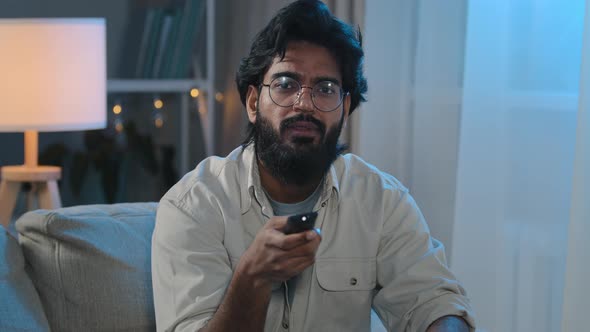 Hispanic Indian Middleaged Adult Bearded Man in Glasses Sits on Sofa at Home in Evening at Night