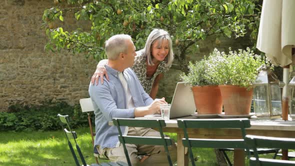 WS, Senior couple at table in garden looking at laptop computer