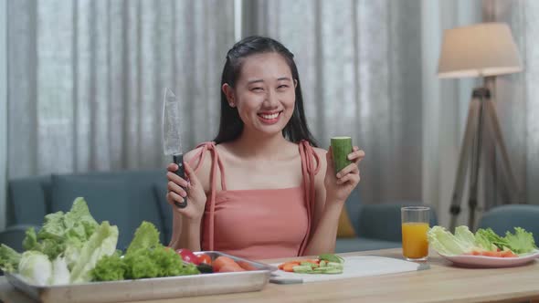 Smiling Asian Woman Holding A Knife And Slicing Cucumber Before Posing To Camera At Home