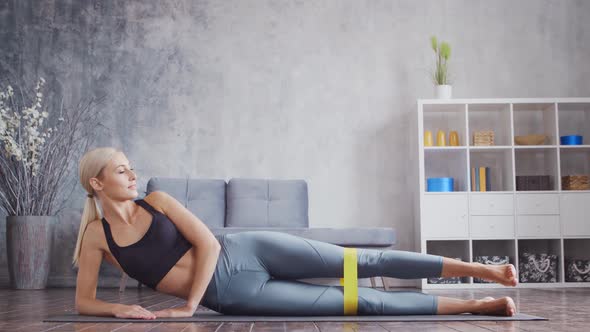 Young and sporty girl in sportswear is doing exercises in home interior using resistance band.