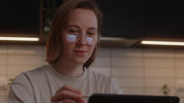 Smiling Girl in Glasses Studying at Home in the Kitchen Using a Tablet and a Digital Pen