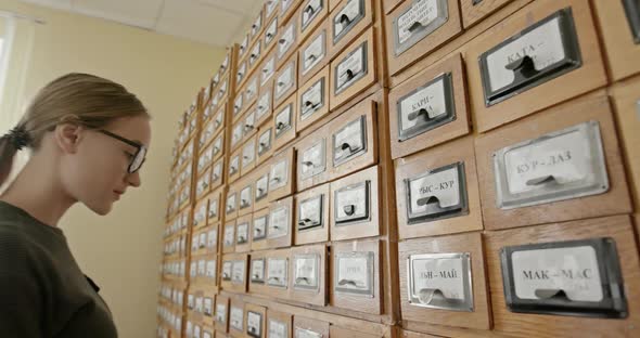 Beautiful Woman in Black Glasses Looks for Information in the Old Library Catalog