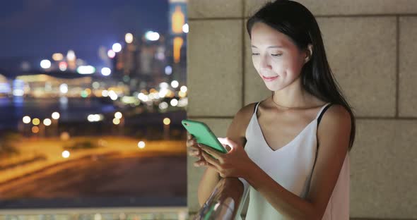 Woman looking at mobile phone with the background of cityscape in Hong Kong 