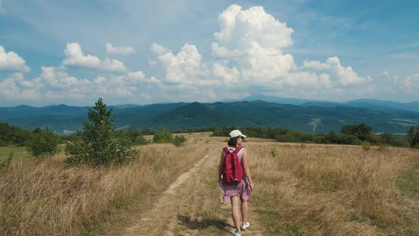 Woman Traveler with a Red Backpack Is Walking on a Mountainous Area