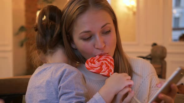 Little Girl Treats Mother with Heart Shaped Lollipop in Cafe