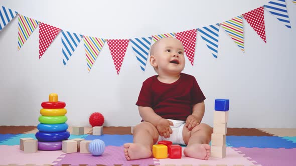 A newborn baby is sitting on foam mats in a game room with various toys