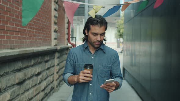 Slow Motion of Attractive Mixed Race Guy Using Smartphone and Holding to Go Coffee Walking Outside