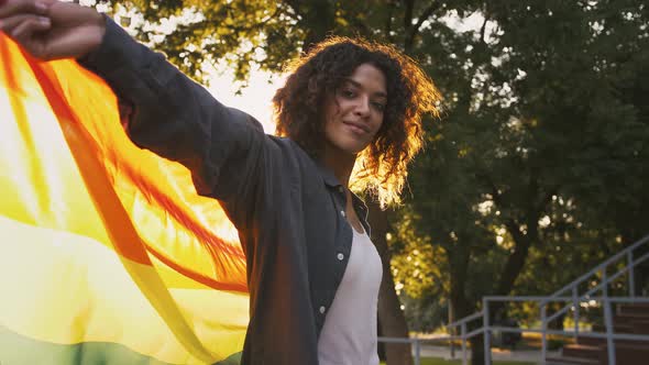 Afroamerican Girl is Smiling and Spinning with Multicolored LGBT Pride Flag While Posing at Sunny