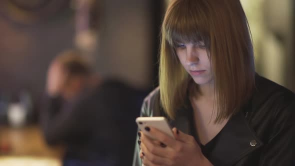 Young Beautiful Redhaired Woman Sitting in Cafe or Bar and Using a Smartphone