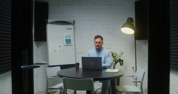 A Young Man Works at a Laptop Sitting Alone in a Meeting Room