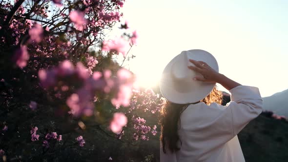 A Young European Woman in a Hat Enjoys a Blooming Wild Rosemary Outdoors on a Sunny Summer Day at