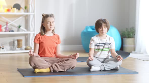 Concentrated Caucasian Girl Sitting on Exercise Mat with Eyes Closed As Boy Repeating Yoga Training