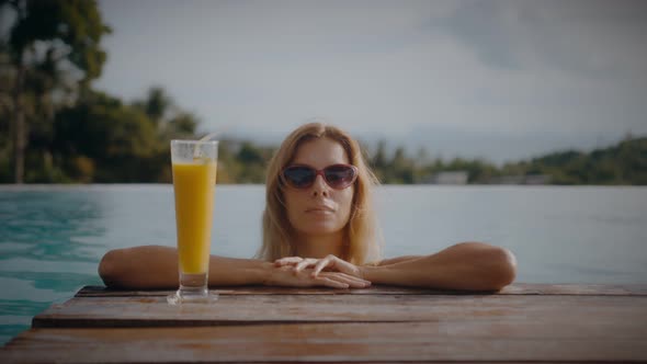 A Blonde Woman Drinks Mango Shake While Lounging in the Sun By the Pool on Vacation