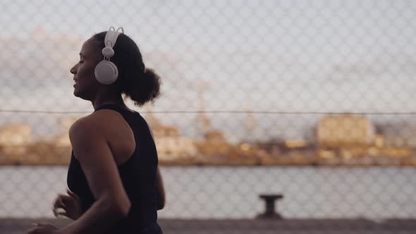 Young Woman In Sportswear And Headphones Running Along Harbour