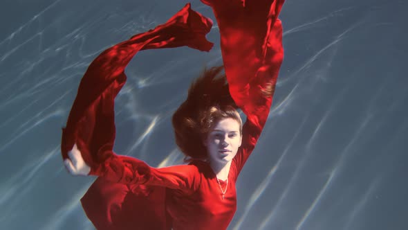 Attractive Redhaired Young Woman Swims Beautifully Underwater in a Red Dress