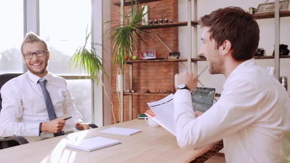 Succesful Caucasian Boss Laughing Smiling with His Subordinate Office Worker Sitting at Table in