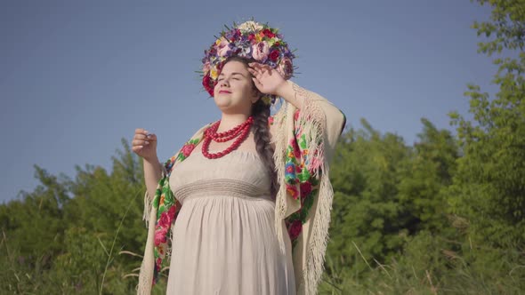 Portrait of Cute Plump Woman with a Wreath on Her Head Smiling in Sunlight on the Green Summer Field