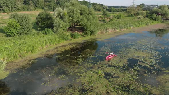 Drone view of woman floating in boat on river. Female is kayaking along beautiful landscape.