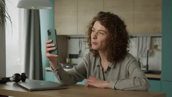 Curly 20s Caucasian Woman Greeting and Talking with Her Friends on a Video Call in Her Apartment