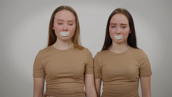 Portrait of Twin Sisters with Taped Mouth Looking at Camera with Sad Facial Expression