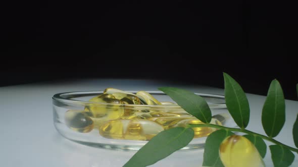 Oil Capsules in Glass Dish and Olive Twig on Glass Table