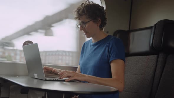 Woman in Glasses Working on a Laptop While Going By Train